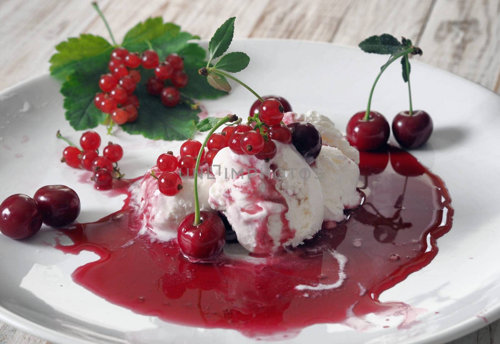 Red cherries and red currants on ice cream with jam in a white plate on a white wooden table.Food background