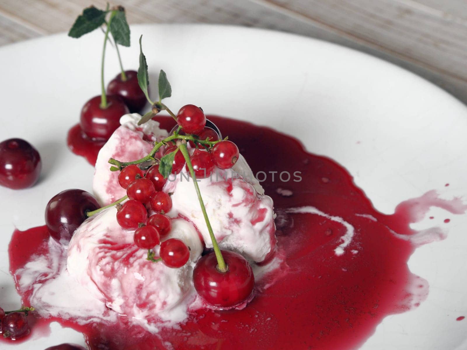 Red cherries and red currants on ice cream with jam in a white plate on a white wooden table.Food background