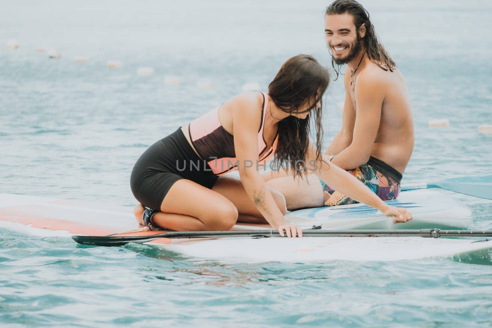 Sea woman and man on sup. Silhouette of happy young woman and man, surfing on SUP board, confident paddling through water surface. Idyllic sunset. Active lifestyle at sea or river