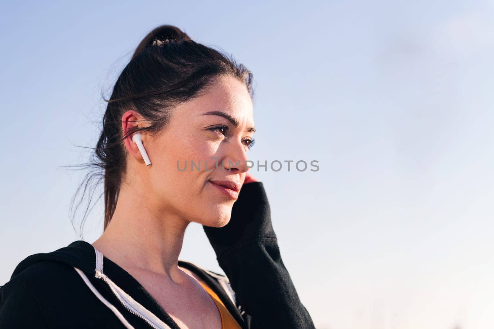 close up portrait of a beauty sportswoman using earphones outdoors in a sunny day, concept of technology and sportive lifestyle, copy space for text