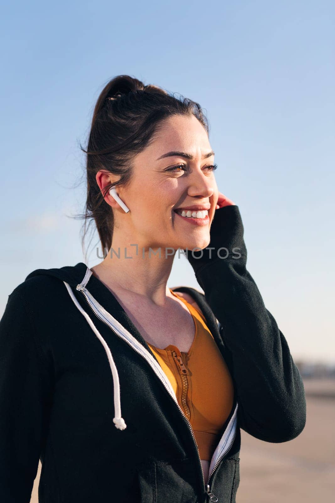vertical portrait of a beautiful sportswoman using earphones outdoors in a sunny day, concept of technology and sportive lifestyle