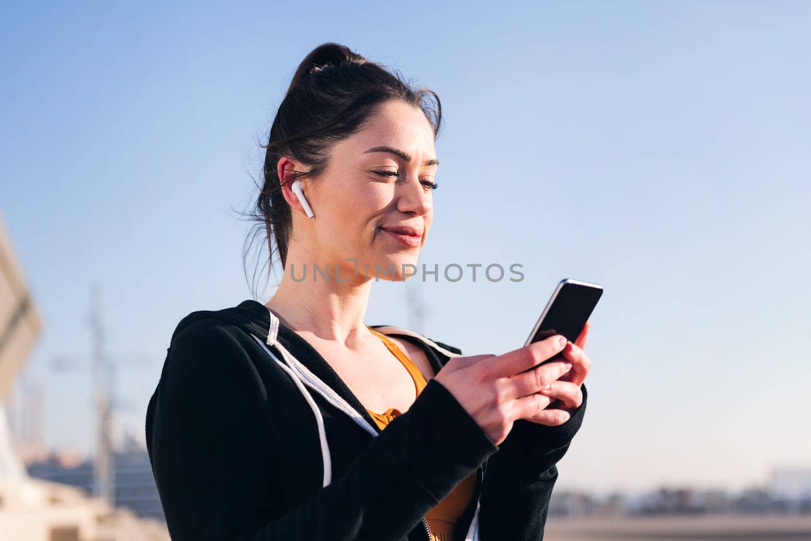 portrait of a beauty female runner playing music on mobile phone using earphones, concept of technology and sportive lifestyle