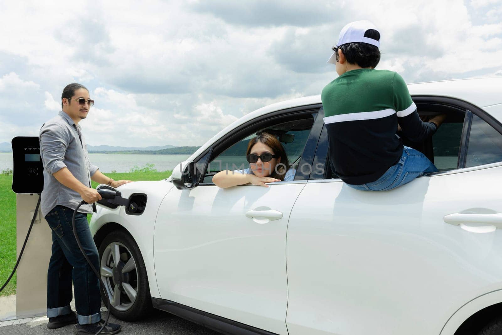 Concept of progressive happy family at green field, lake with electric vehicle. by biancoblue