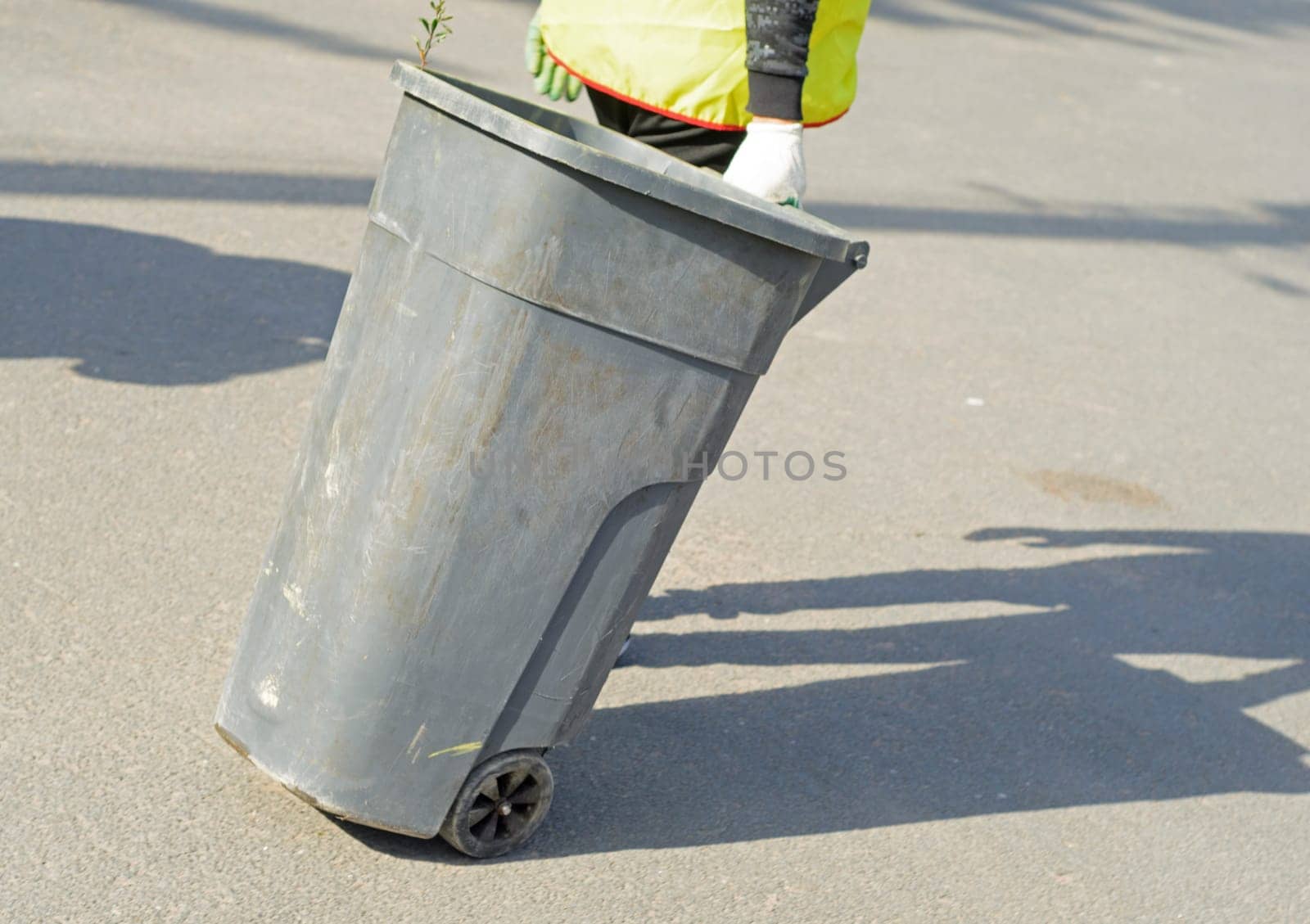 A cleaner carries a dumpster down the street.Regular garbage collection