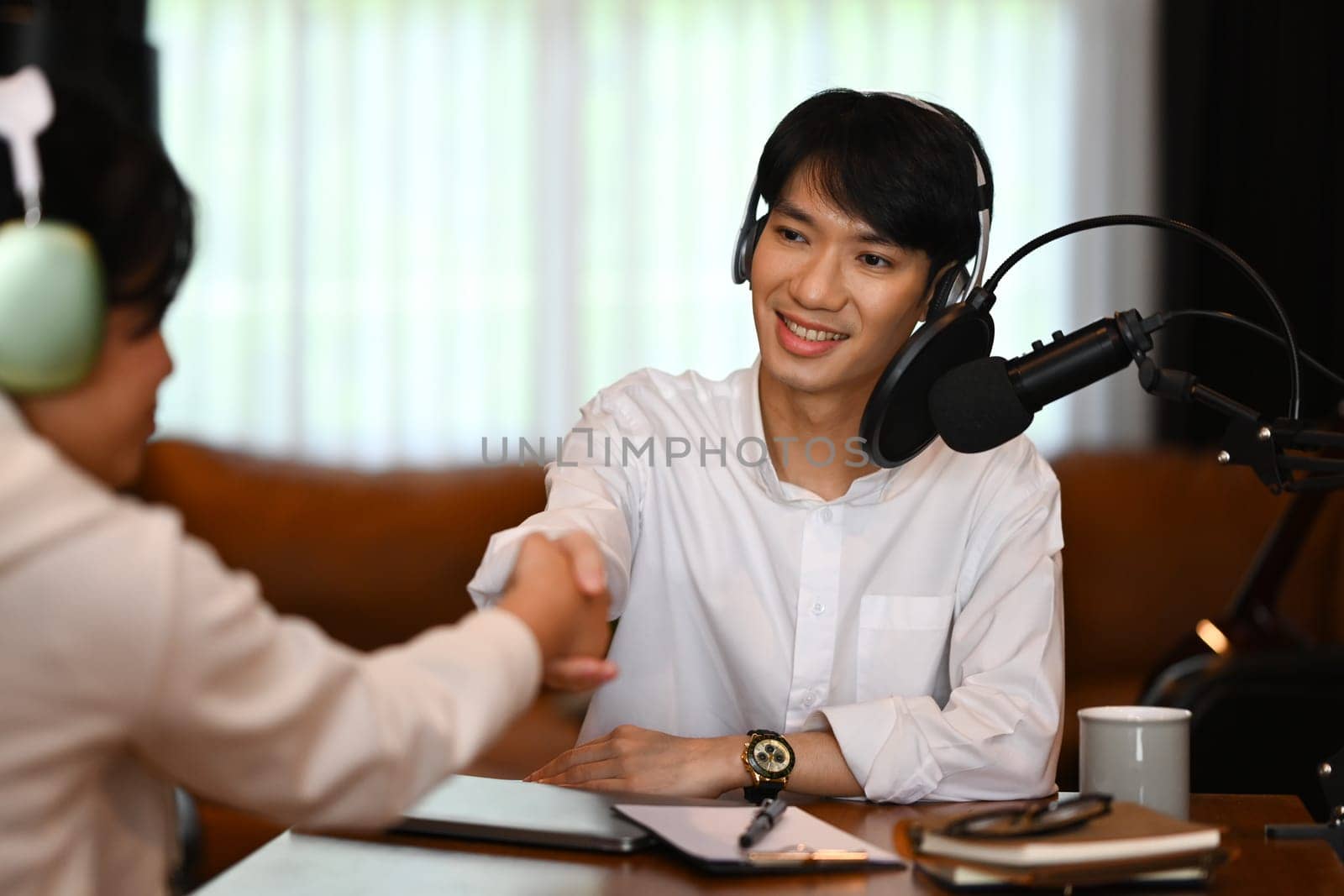 Smiling radio host shaking hands with her guest after interviewing. Podcasts and technology concept.
