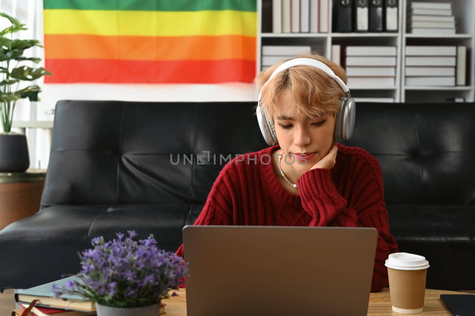 Young gay man wearing headphone and using laptop, communicating online, working remote from home by prathanchorruangsak