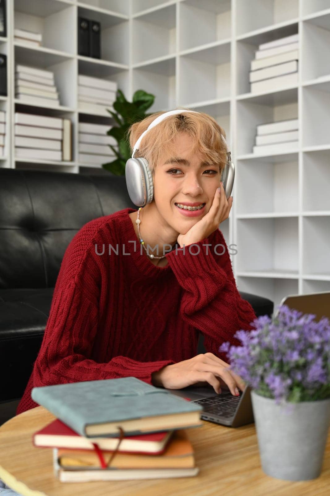 Stylish young gay man in wireless headphones listening to music and looking away.