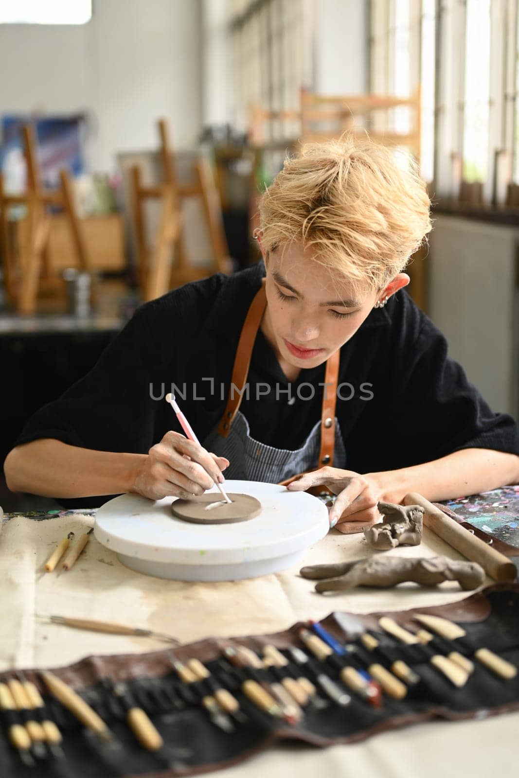 Focused man pottery artist decorating clay plate on table at ceramic workshop. Indoors lifestyle activity and hobbies concept by prathanchorruangsak