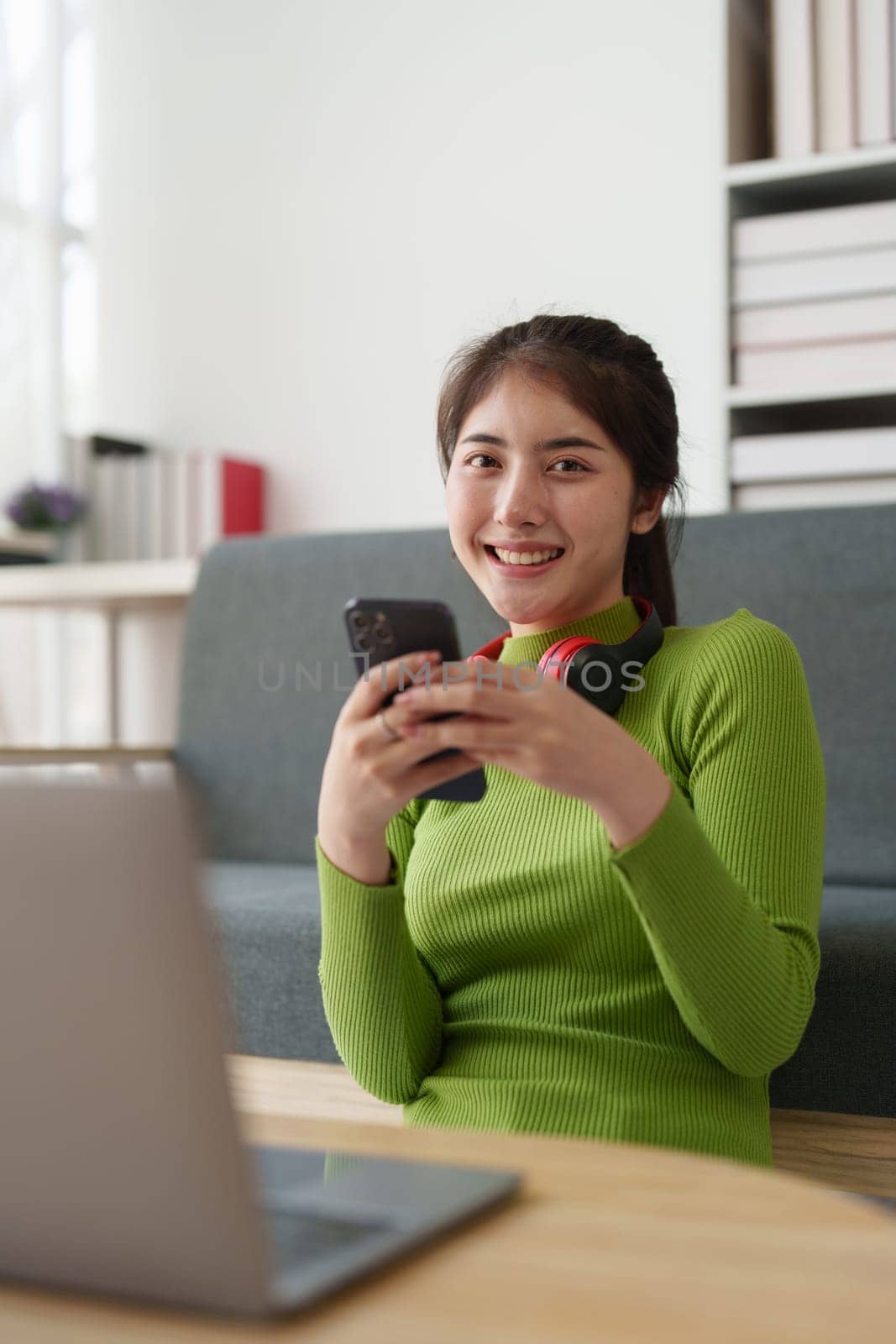 Young asian relaxed smiling pretty woman relaxing with mobile phone at home. Female feeling joy enjoying with mobile phone on cozy couch.