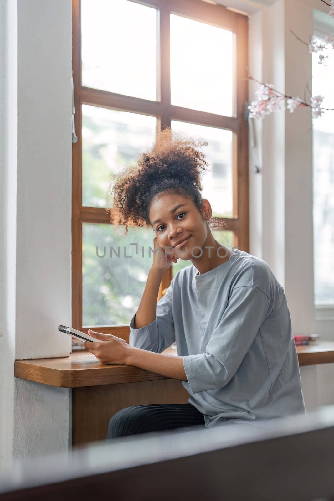 Smiling young black woman freelancer working from home, sitting on couch. Relaxed african american lady enjoying her weekend.