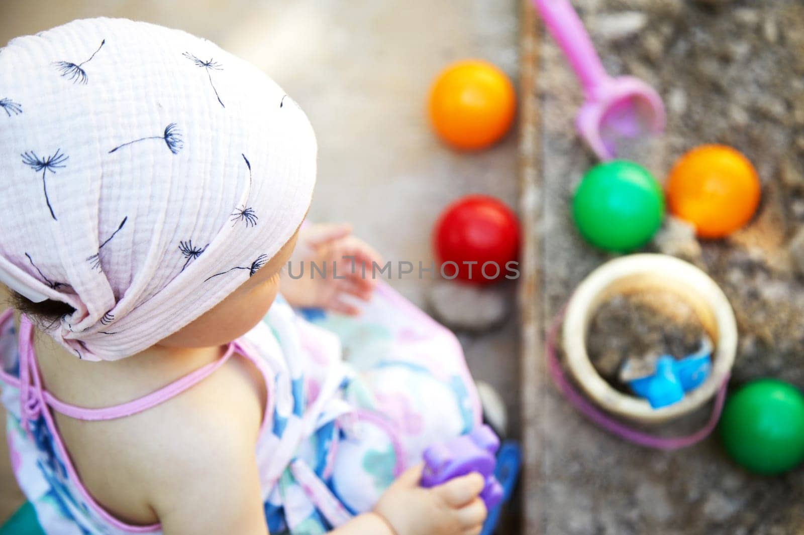 toddler girl playing in sand in sandbox with various toys on outdoor playground