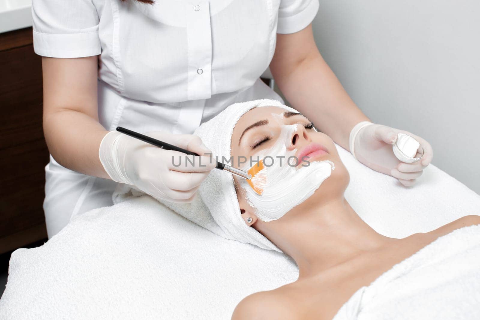 beautician applies the mask to the face of beautiful young woman in the spa salon. spa treatments