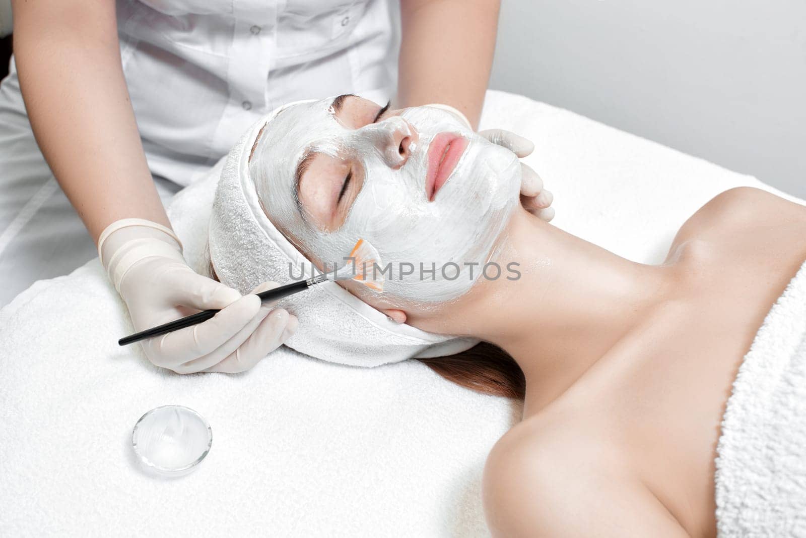 beautician applies the mask to the face of beautiful young woman in the spa salon. spa treatments closeup