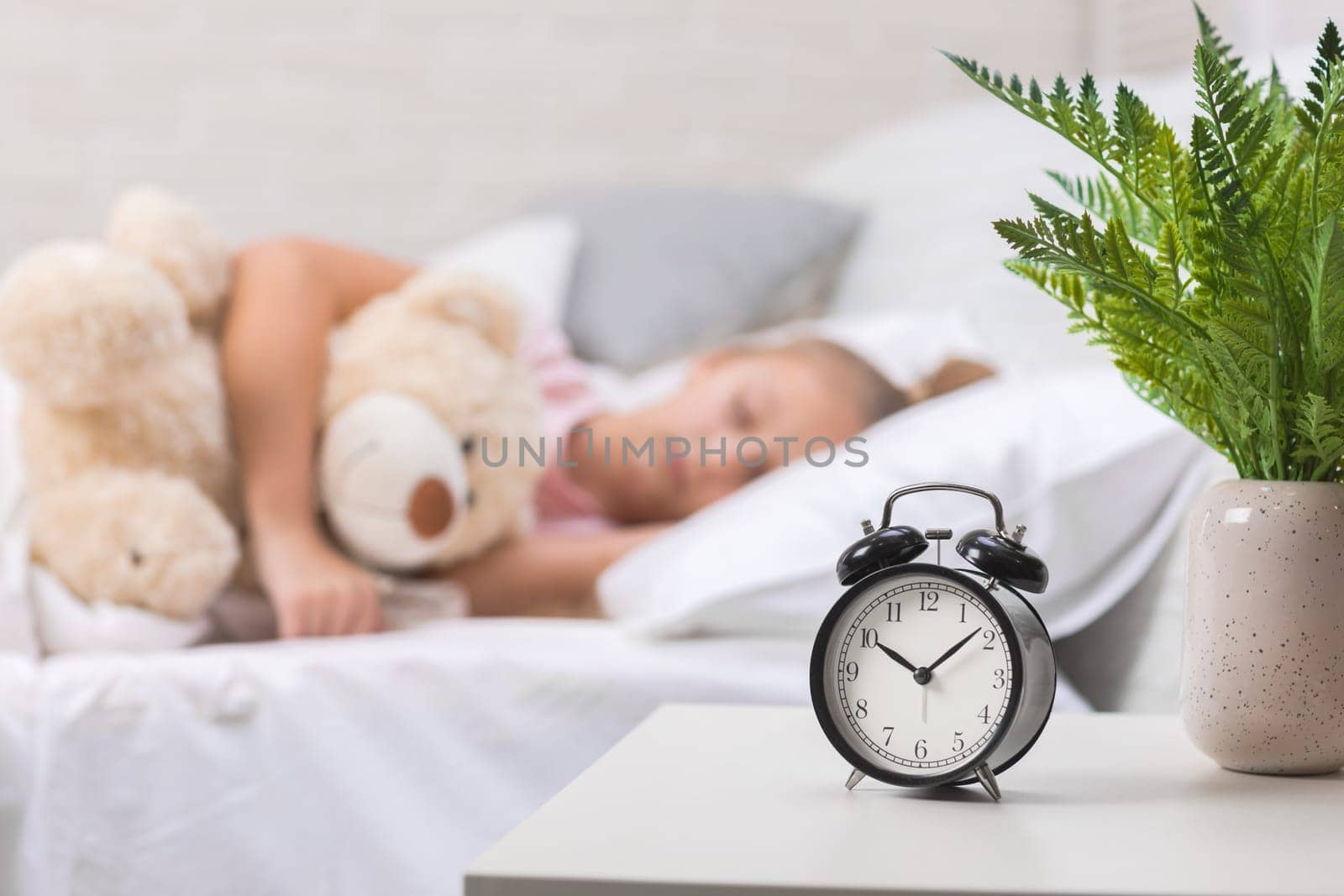 Cute little child girl sleeping with teddy bear in her bed. focus on clock