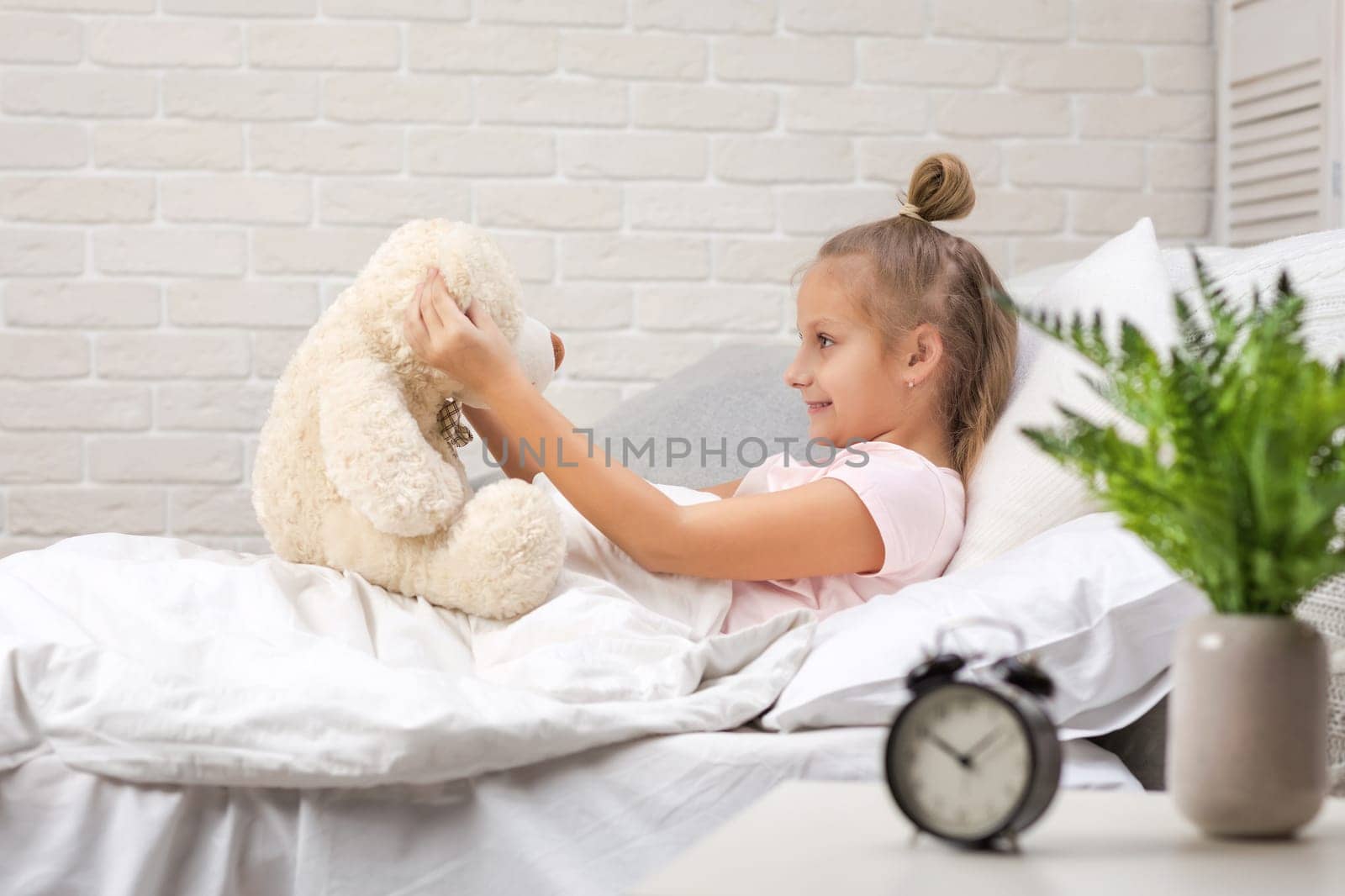 adorable little child girl playing with teddy bear in bed in morning