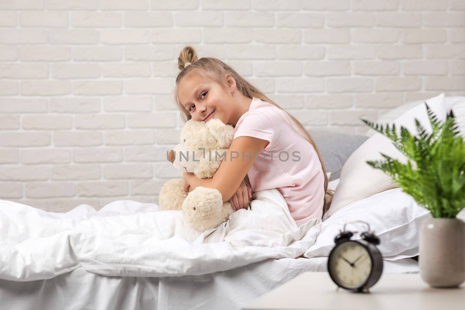 adorable little child girl playing with teddy bear in bed in morning. baby hugging a teddy bear