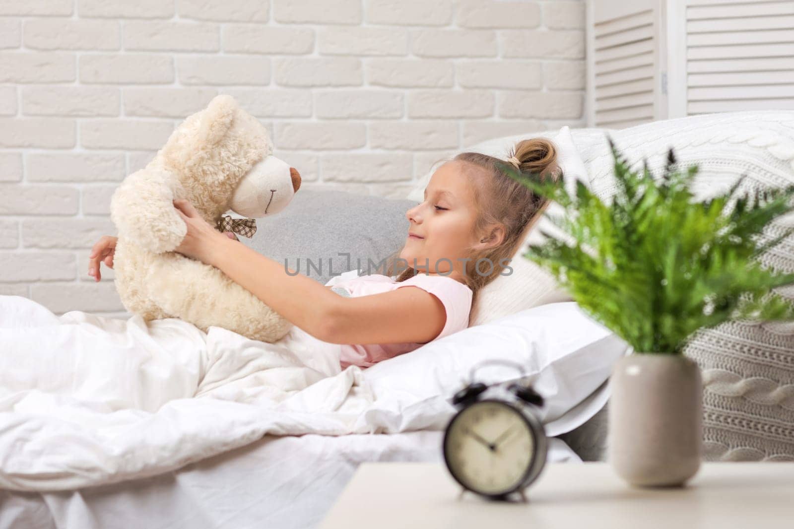 adorable happy little child girl playing with teddy bear in bed in morning.
