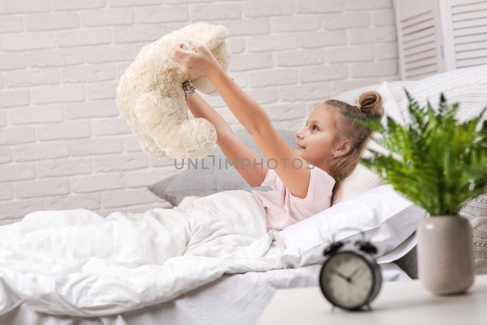 adorable little child girl playing with teddy bear in bed in morning