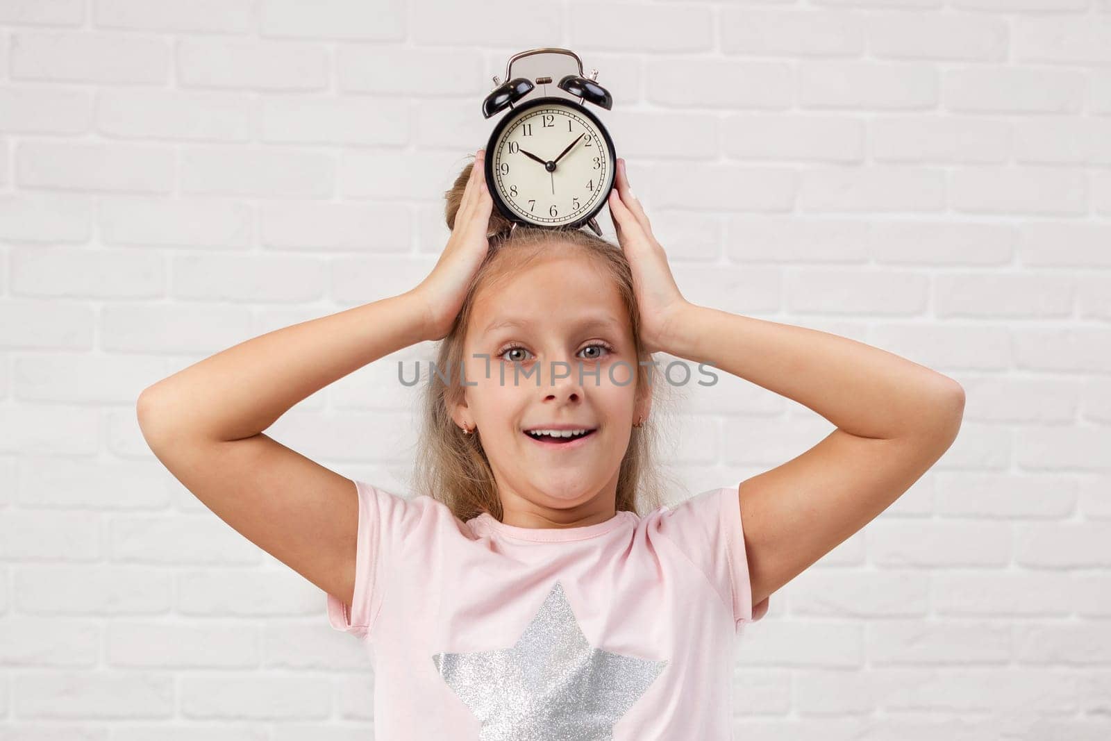 cute surprised little child girl in pyjamas with clock in bed. good morning