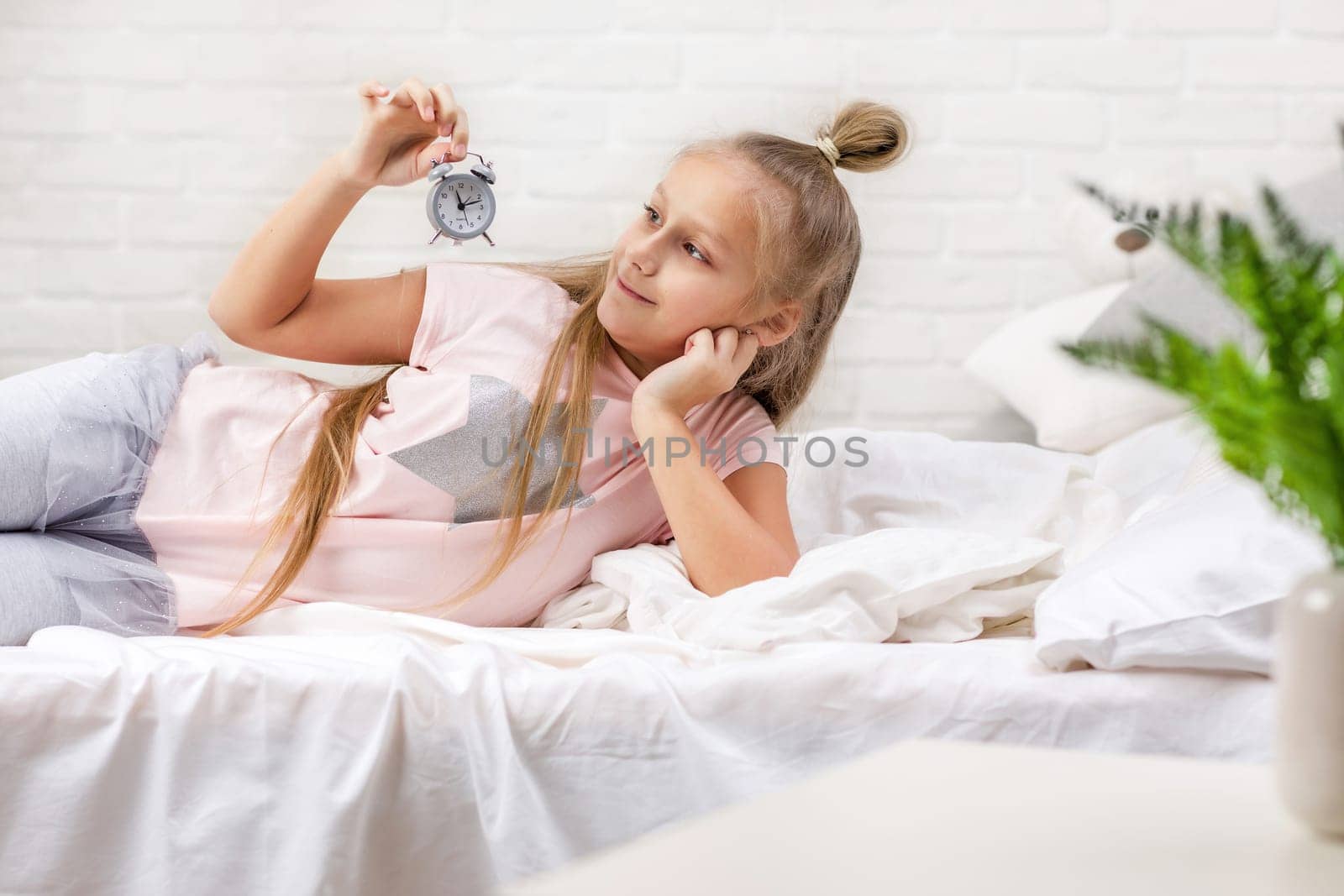 cute little child girl in pyjamas with clock in bed. good morning