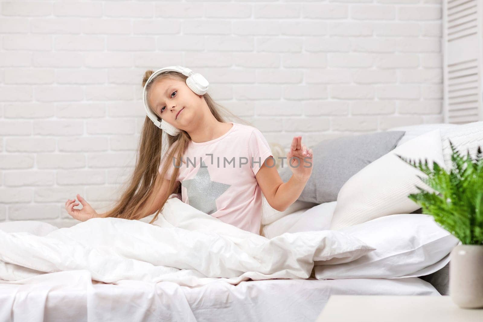 smiling little child baby girl listening to the music with the headphones and dancing on bed. happy morning