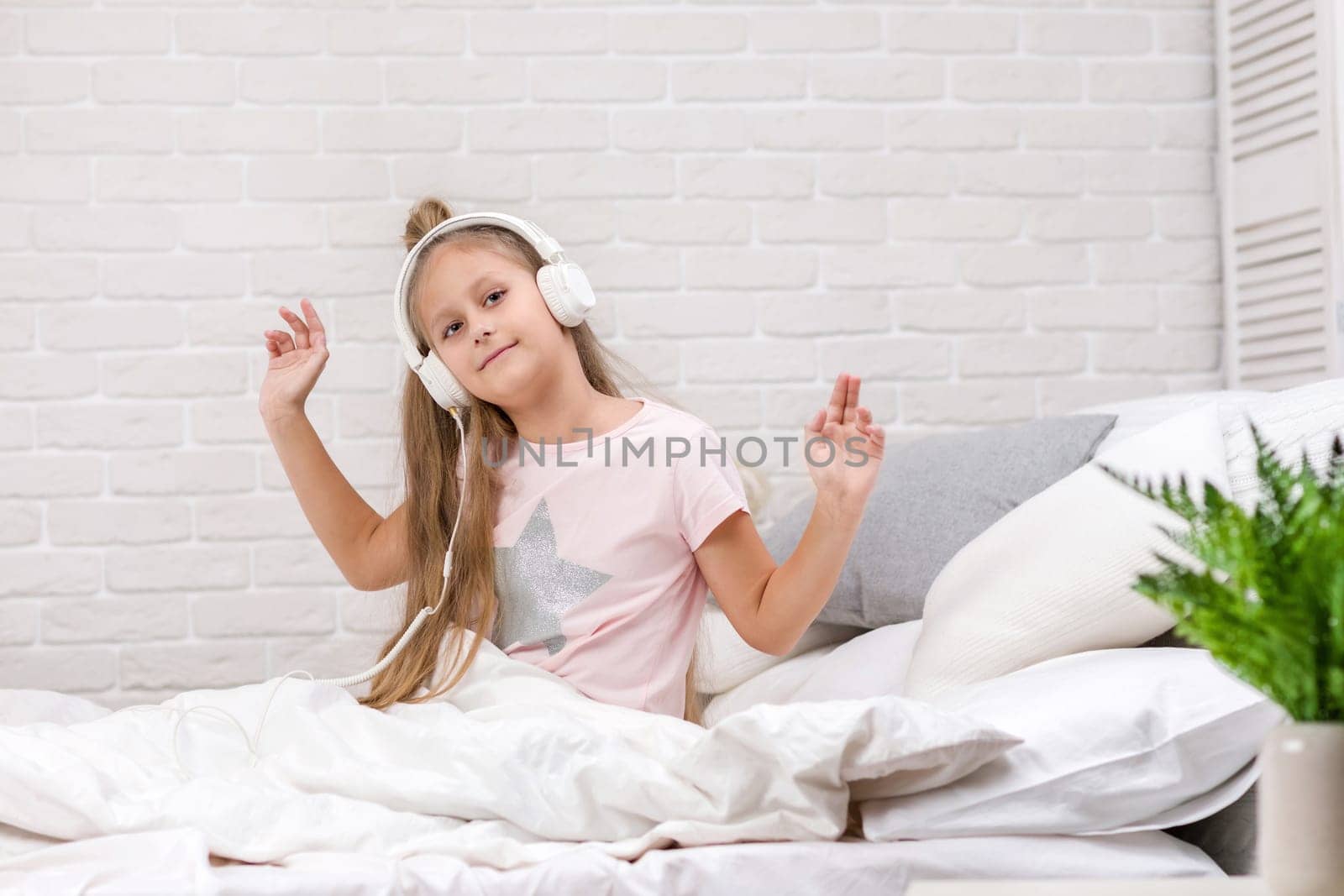 happy little child baby girl listening to the music with the headphones and dancing on bed. happy morning
