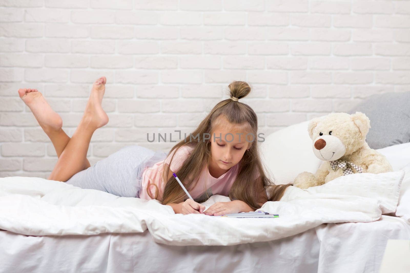 cute little girl drawing pictures while lying on bed. Kid painting at home