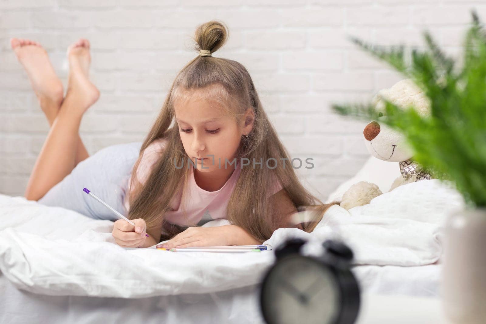 cute little girl drawing pictures while lying on bed. Kid painting at home