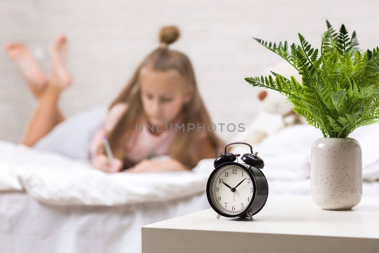 cute little girl drawing pictures while lying on bed. Kid painting at home