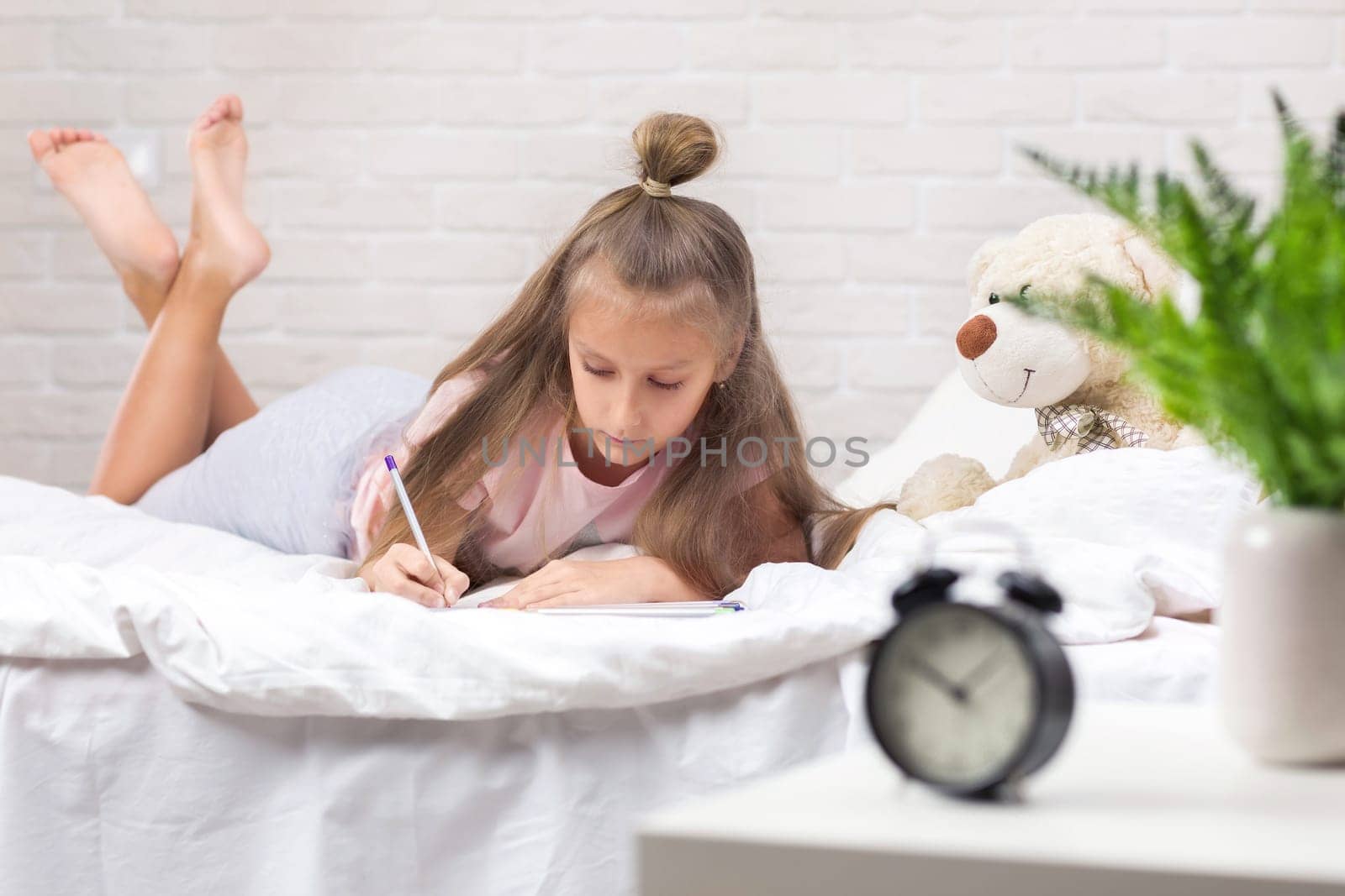 cute little girl drawing pictures while lying on bed. Kid painting at home