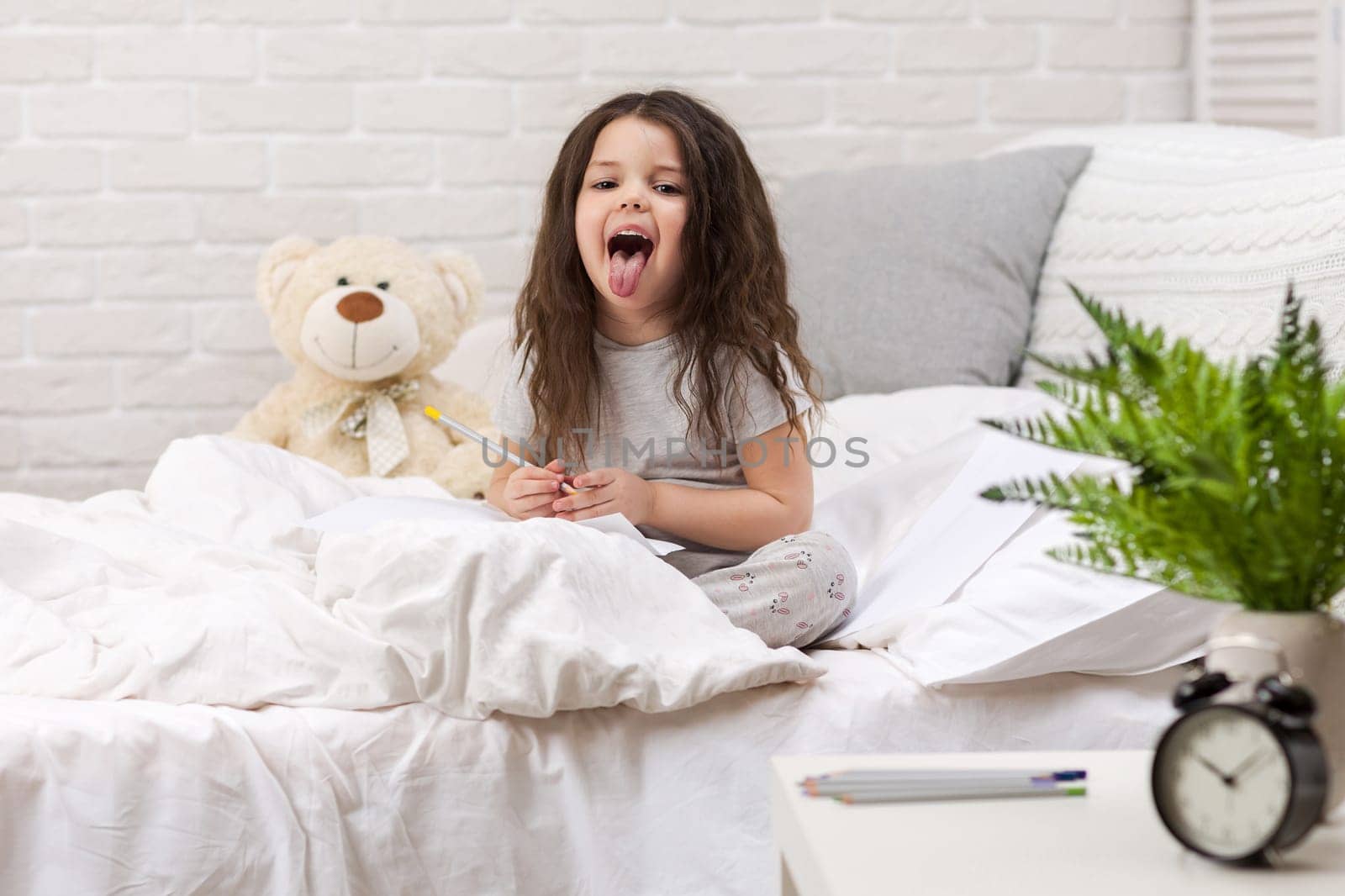 cute little girl drawing pictures while lying on bed. Kid fooling around