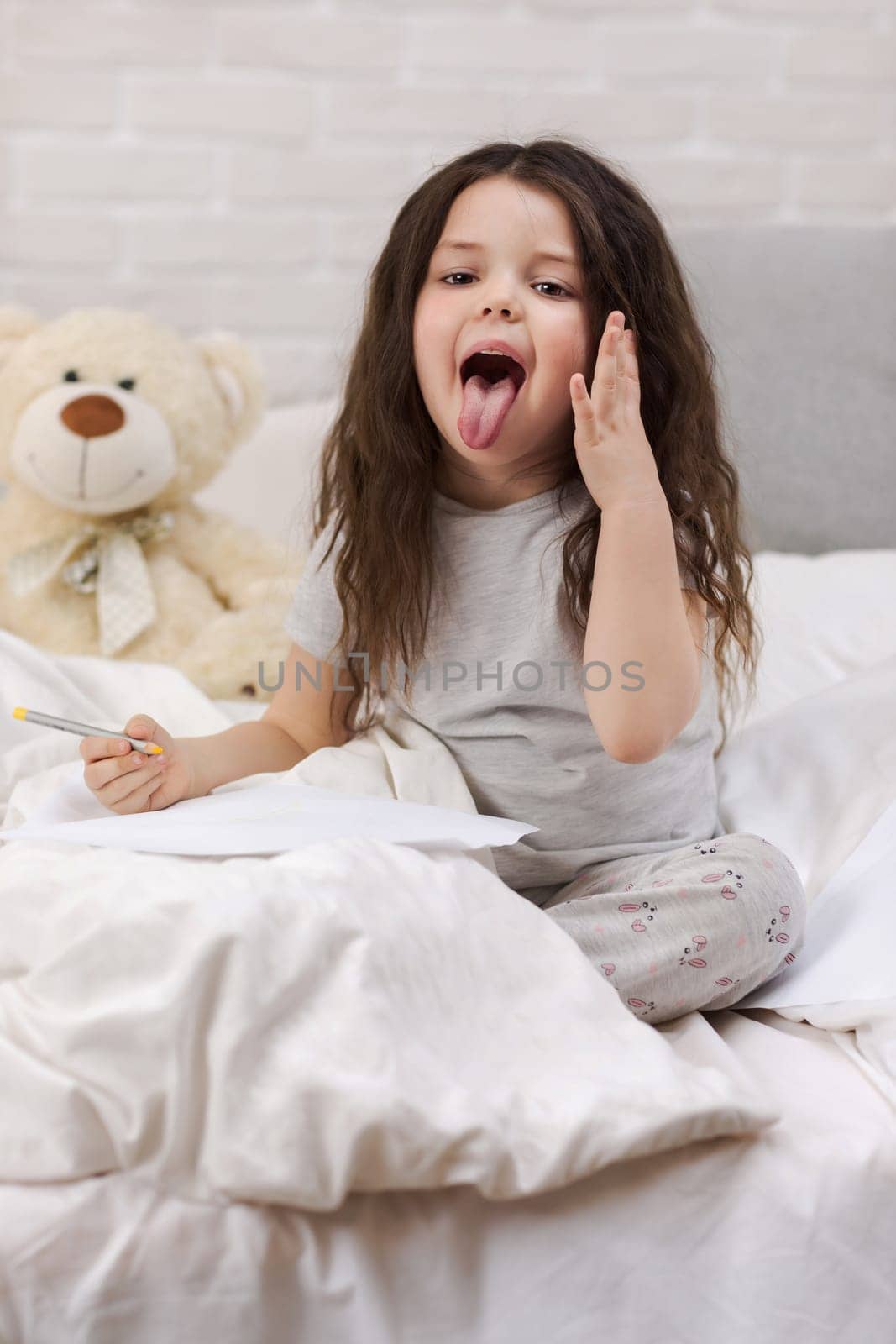 cute little girl drawing pictures while lying on bed. Kid fooling around