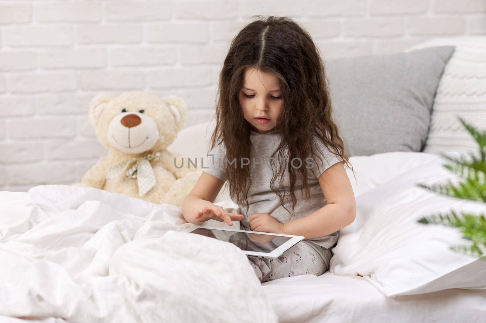 cute little child girl lies in bed uses digital tablet. child playing on tablet pc.