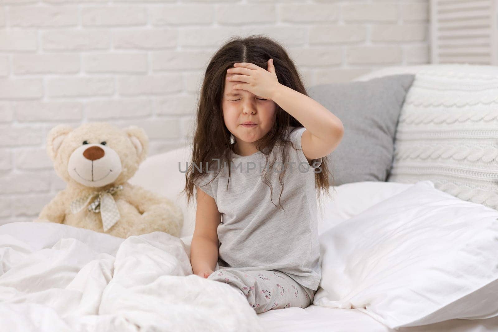 Sick little child girl lying in bed. Cold flu season. headache