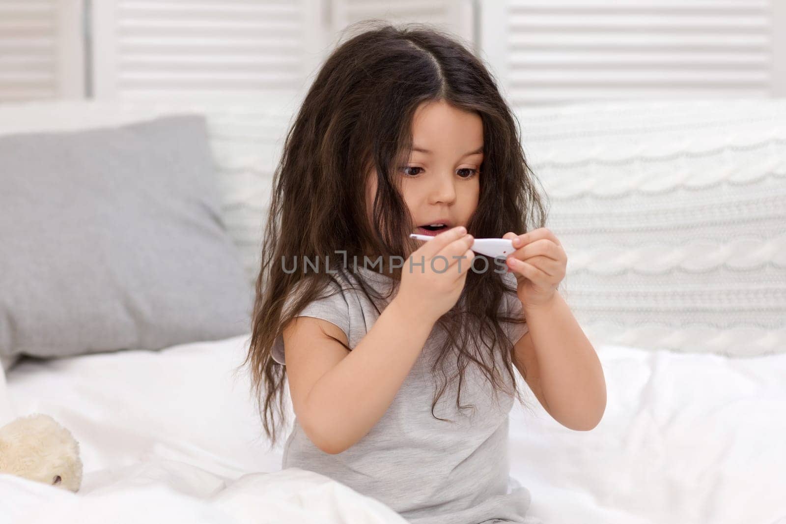 Sick little child girl lying in bed with thermometer. Cold flu season