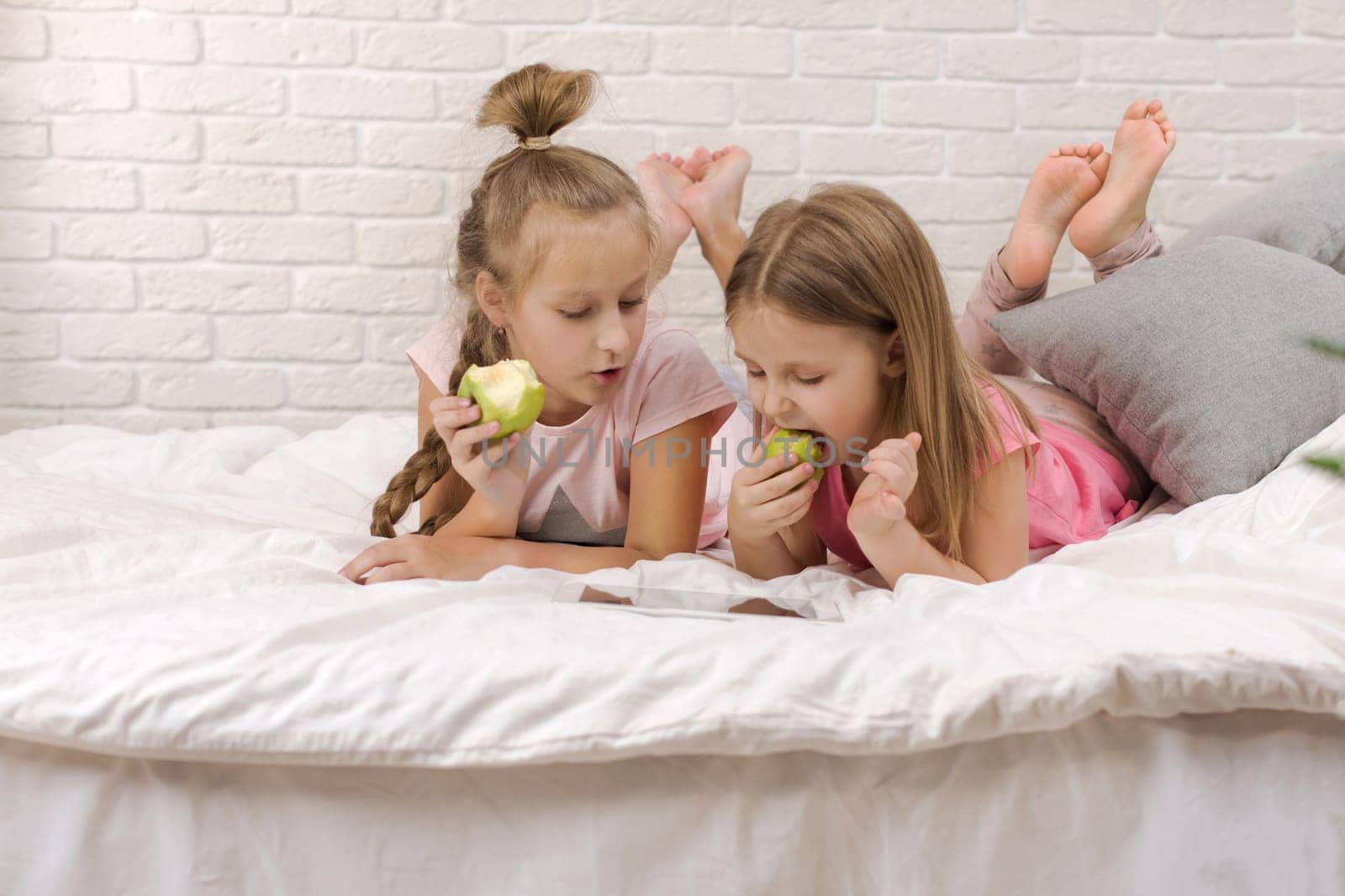 two cute children girls use digital tablet in bed. child playing on tablet pc.