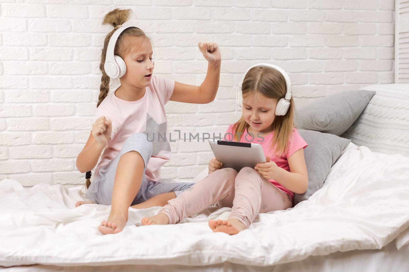 two cute children girls playing in the bedroom. two cute children girls use digital tablet in bed.