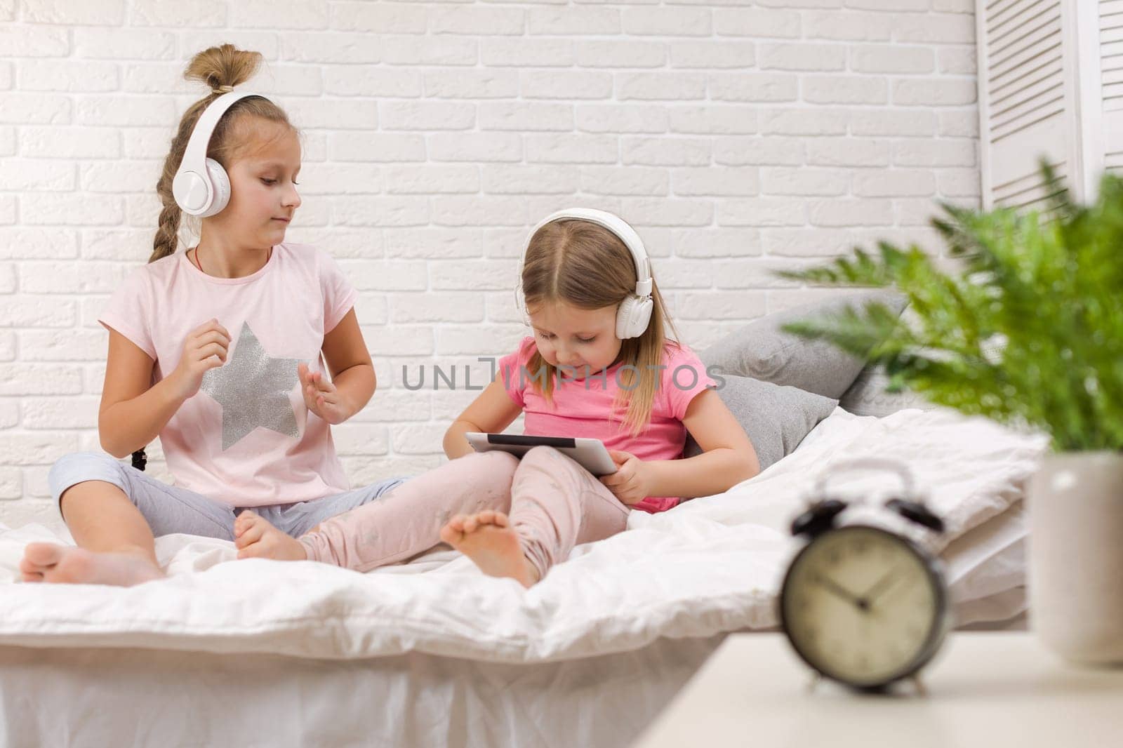 two cute children girls playing in the bedroom. two cute children girls use digital tablet in bed.