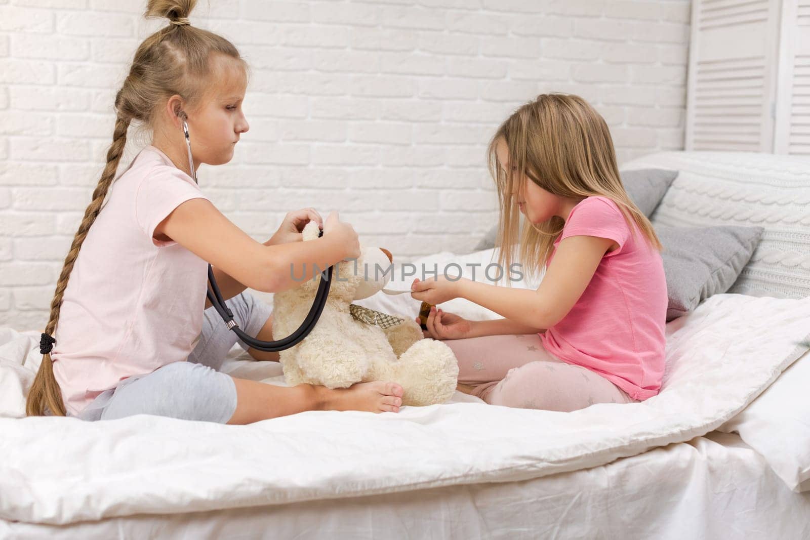two cute children girls playing doctor with teddy bear at home. girl listens a stethoscope to toy.