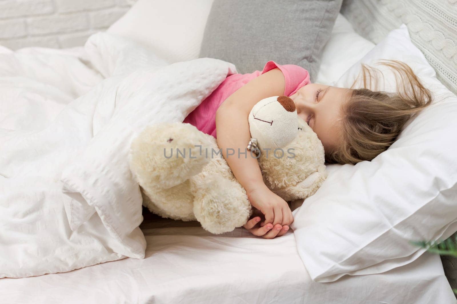 Cute little child girl sleeping with teddy bear in her bed