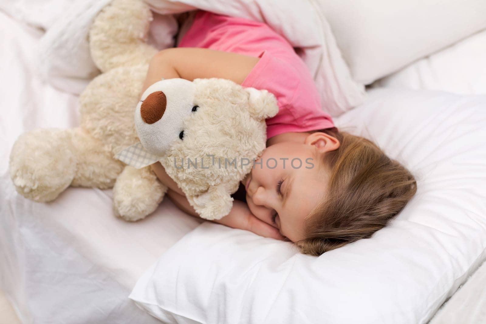 Cute little child girl sleeping with teddy bear in her bed