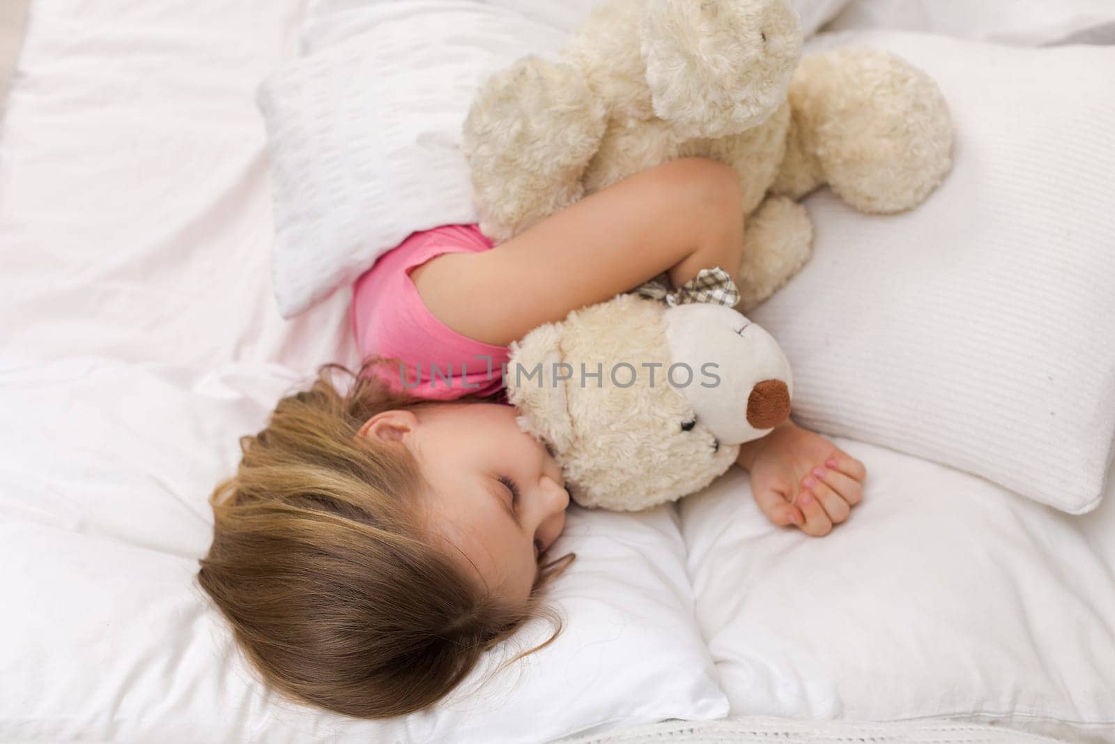 Cute little child girl sleeping with teddy bear in her bed