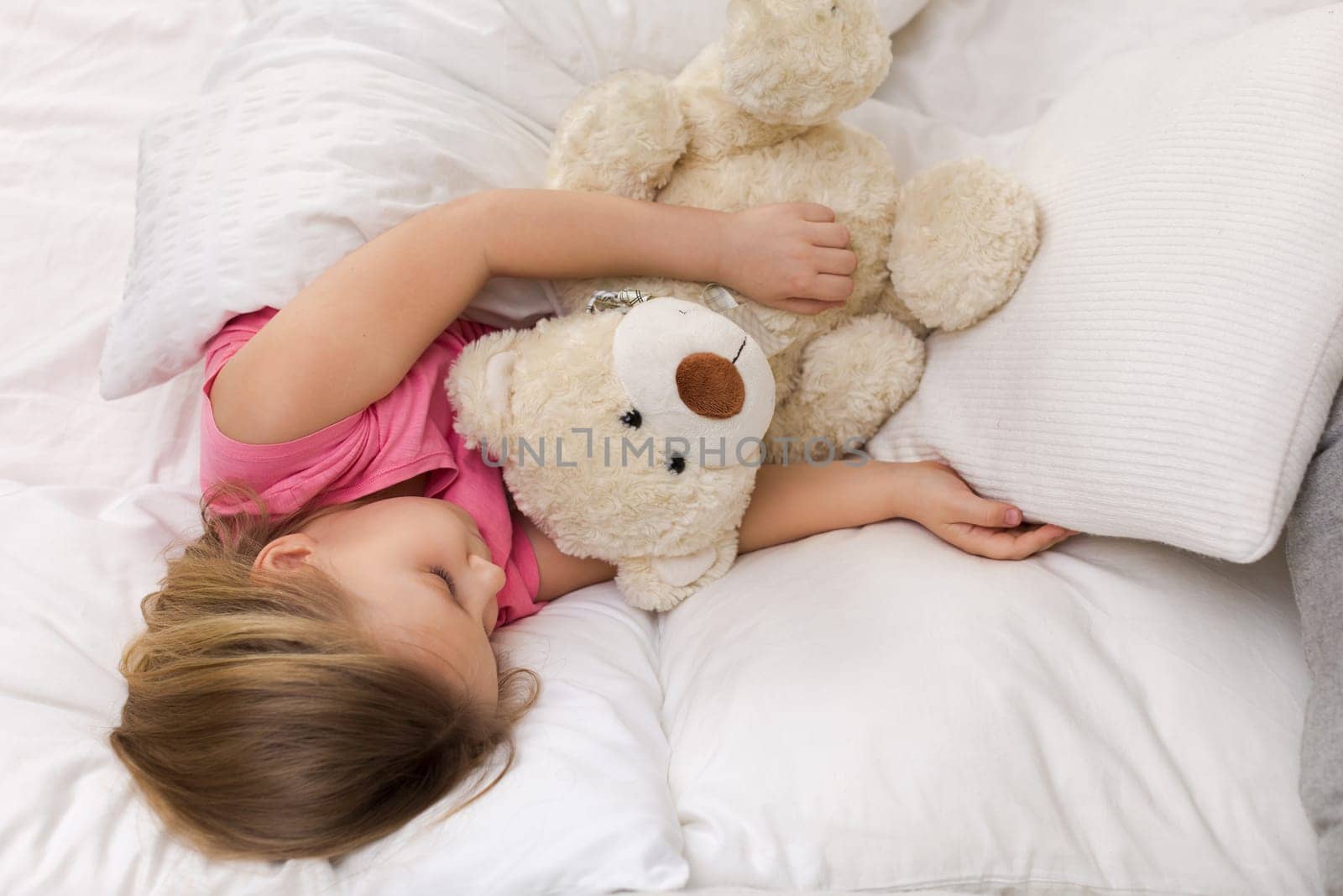 Cute little child girl sleeping with teddy bear in her bed