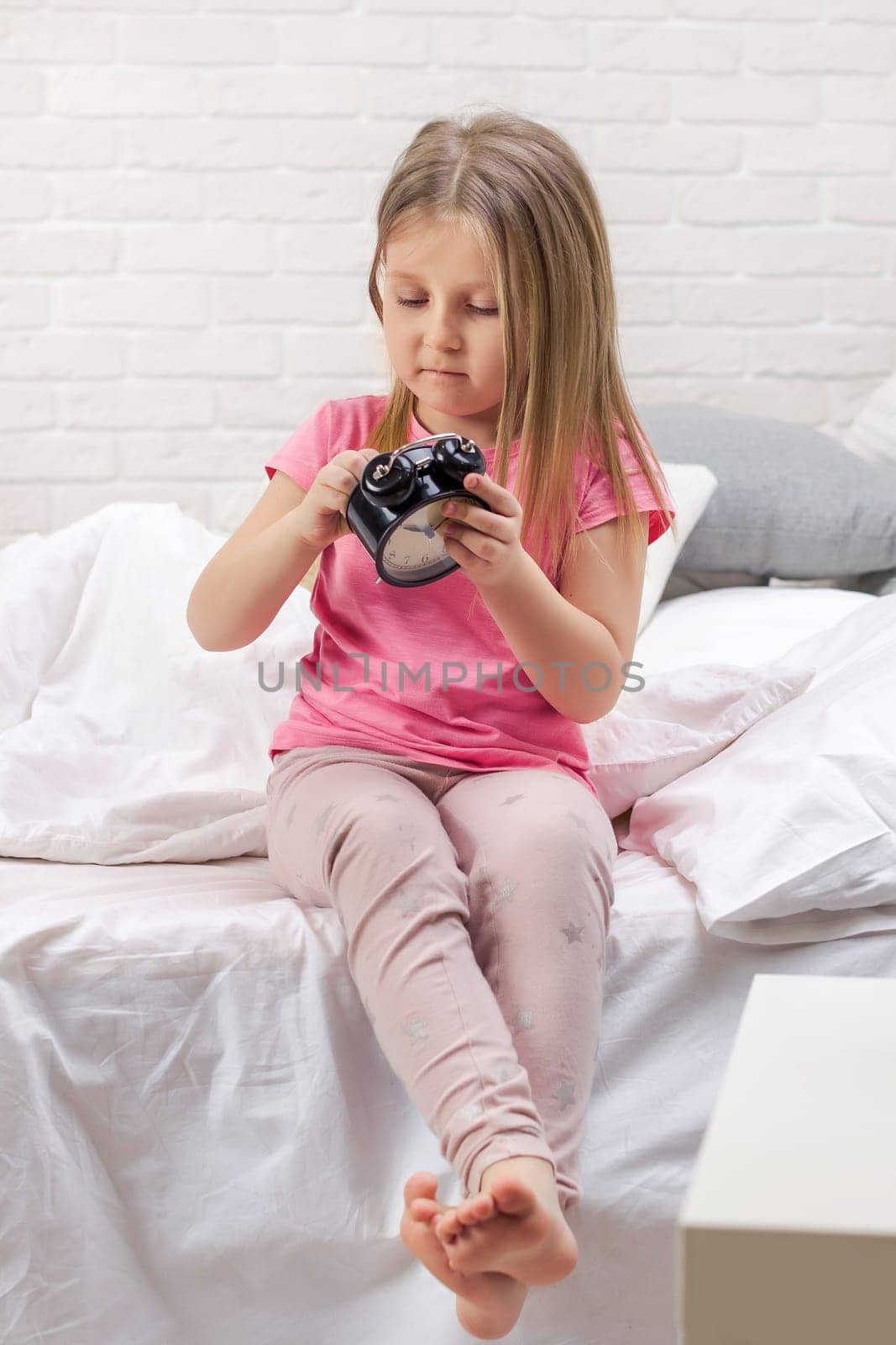 cute little child girl in pyjamas with clock in bed. good morning