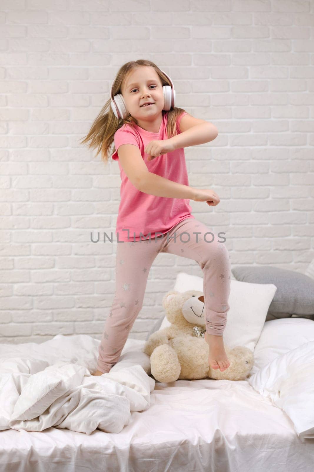 little child baby girl listening to the music with the headphones and dancing on bed. happy morning
