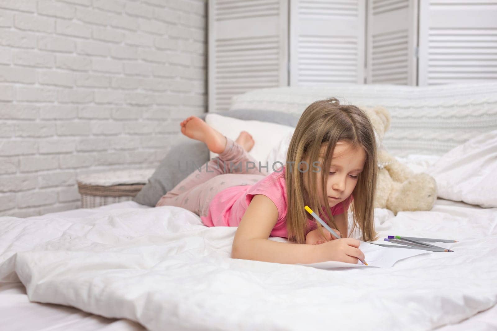 cute little girl drawing pictures while lying on bed. Kid painting at home