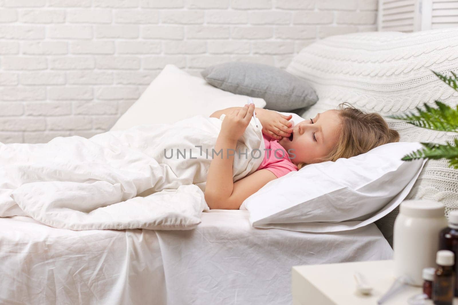 Sick little child girl lying in bed with thermometer. Cold flu season