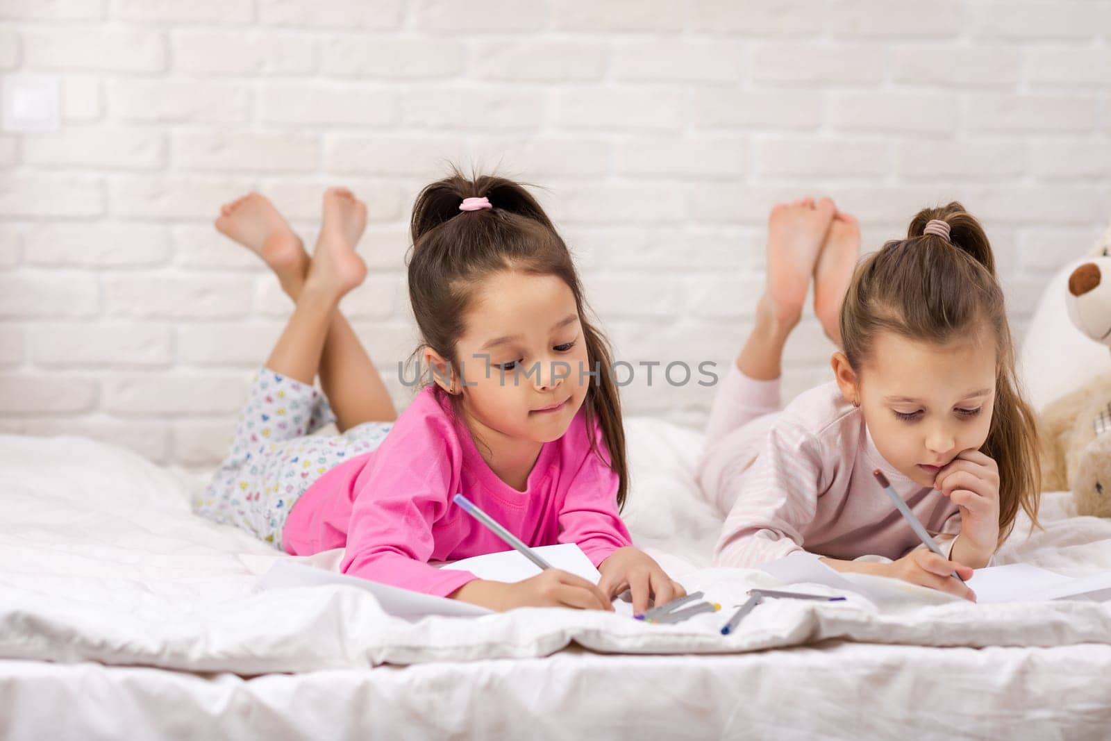 kids drawing pictures while lying on bed. pajama party and friendship.