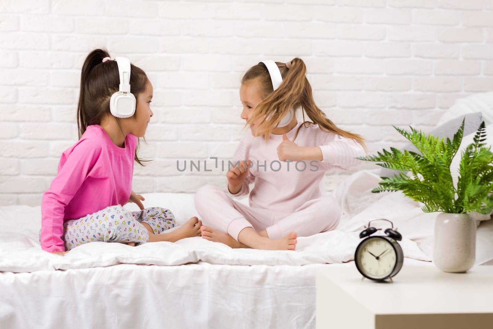 little children girls listening to the music with the headphones and dancing on bed. pajama party and friendship.