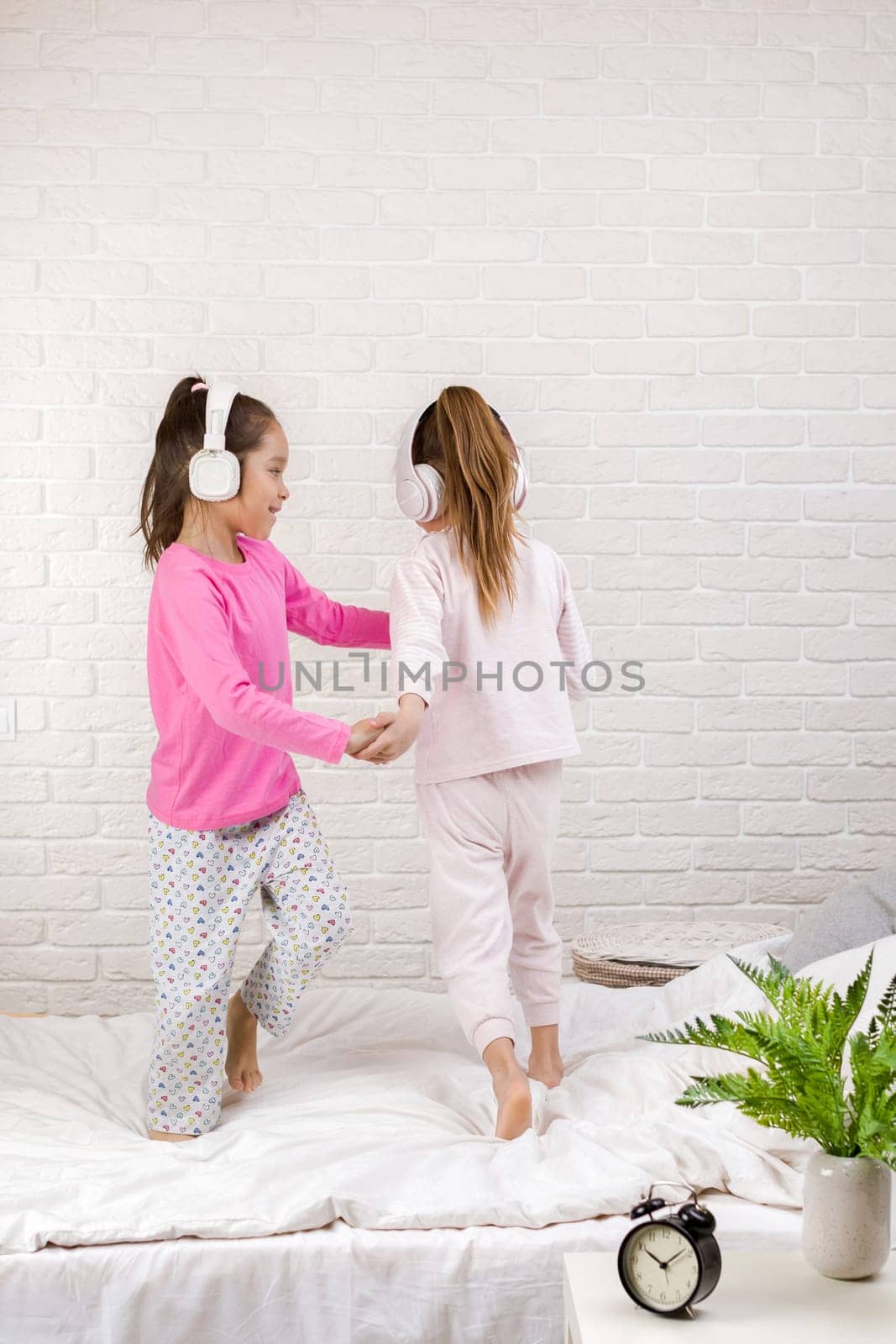 little children girls listening to the music with the headphones and dancing on bed. pajama party and friendship.